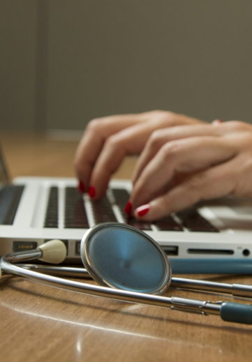 person sitting while using laptop computer and green stethoscope near